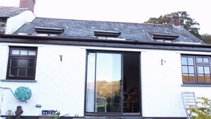 Un bâtiment blanc avec un toit recouvert de tuiles, une porte-fenêtre coulissante et un petit porche.