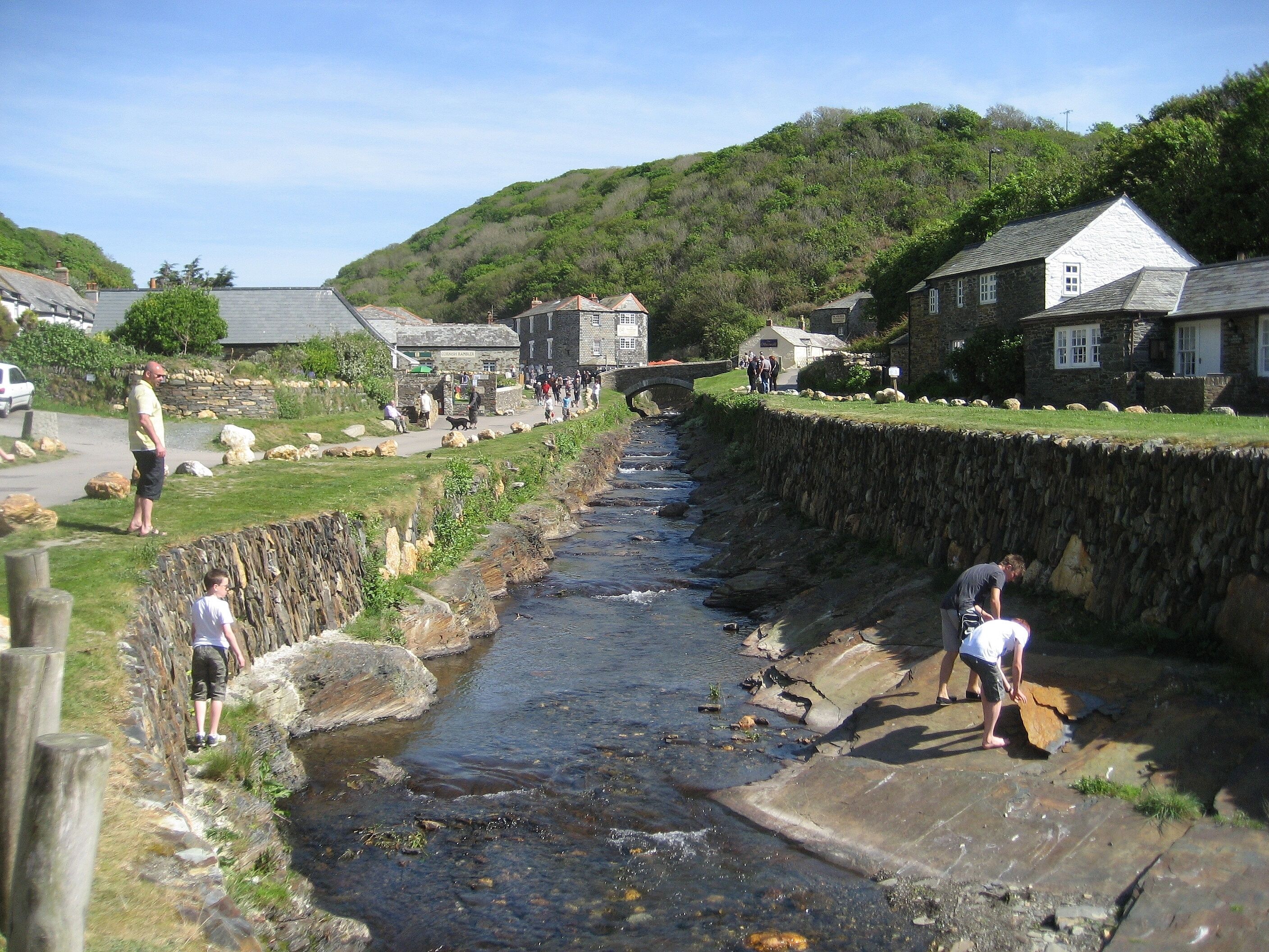 A narrow water channel with people walking along the banks, surrounded by stone walls and houses.