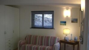 A room with a striped sofa, a small table with a lamp, a cabinet, and a window with blinds. - Apartment/ flat - Monte argentario (Monte Argentario)
