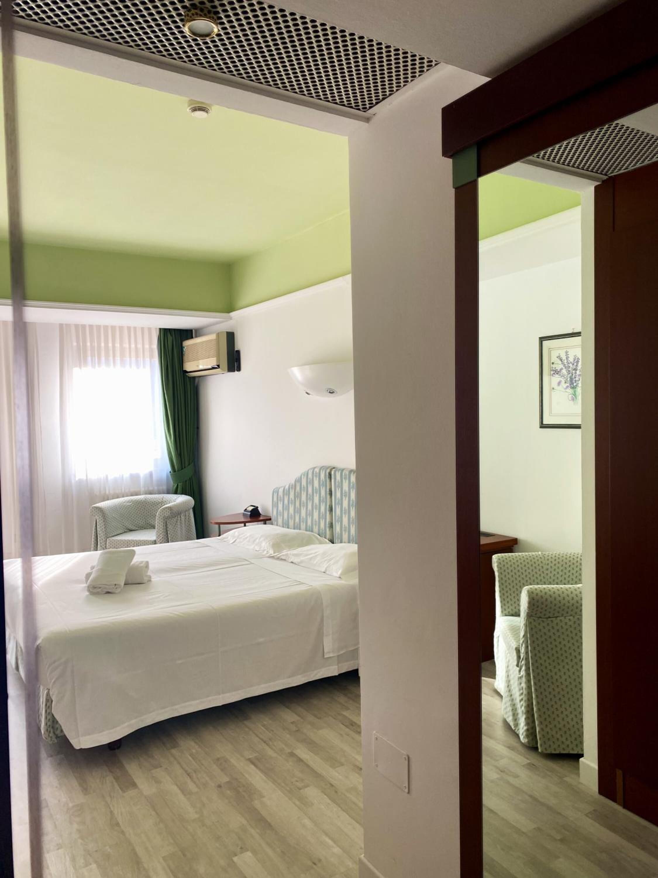 Una camera d'albergo con un letto, una sedia, una scrivania e un quadro appeso al muro.