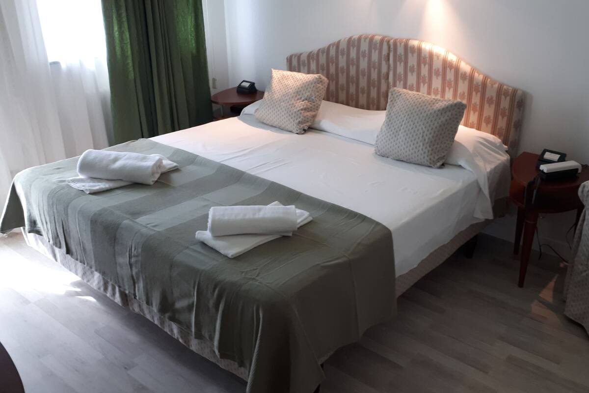 A neatly made bed with pillows and towels, a bedside table with a phone, and a chair in a hotel room.