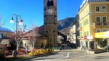 Una strada acciottolata con una storica torre dell'orologio, un edificio giallo con un cartello e un cielo azzurro limpido.