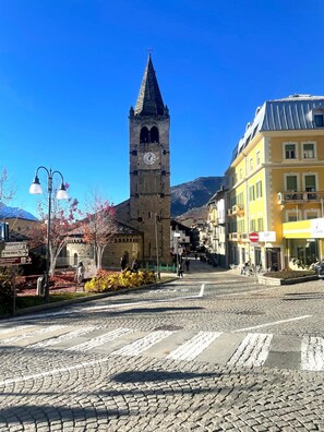 A cobblestone street with a historic clock tower, a yellow building with a sign, and a clear blue sky.