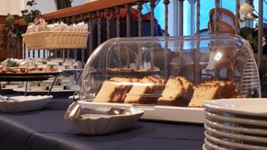 A buffet table with a variety of food items, including a covered display case with bread and a basket of pastries.