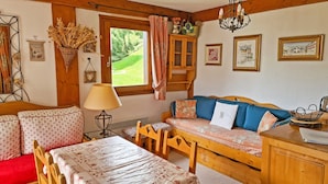 A cozy room with a wooden sofa, a dining table, and a window with curtains.