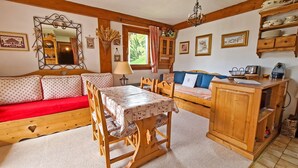 A cozy room with a wooden sofa, a dining table, and a kitchen area.
