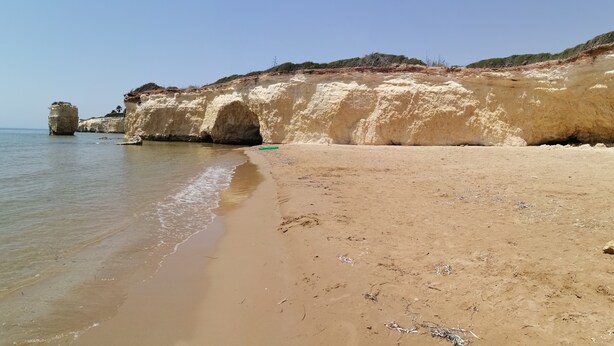 Una playa arenosa con un acantilado grande y una pequeña estructura parecida a una cueva.