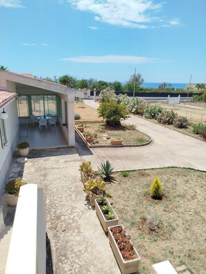 A modern building with a covered patio, outdoor seating, and a landscaped garden with various plants.