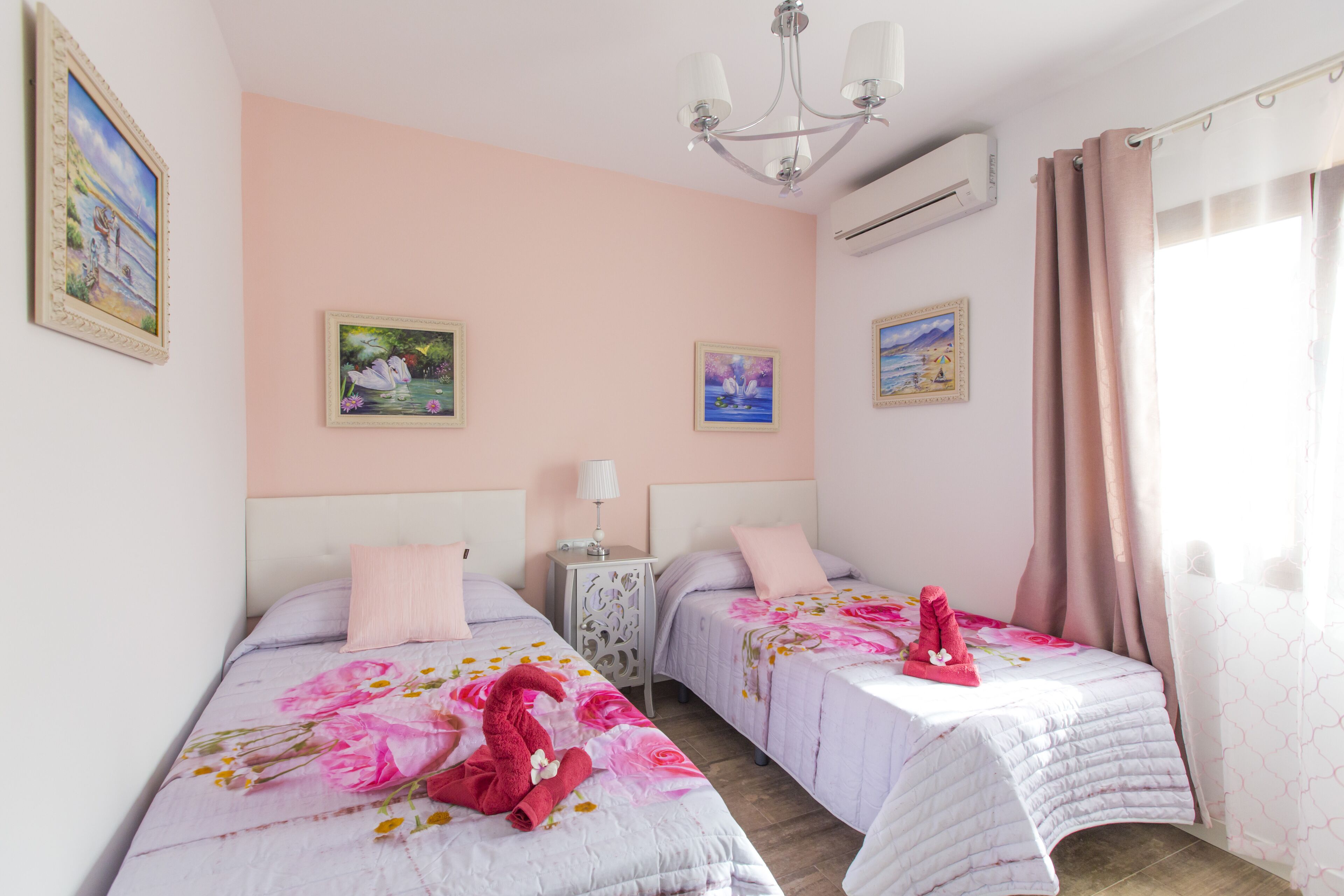 Une chambre d’hôtel avec deux lits, un lustre et des œuvres d’art accrochées aux murs.