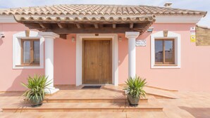 Un bâtiment avec un toit recouvert de tuiles, une porte en bois et deux plantes en pot placées sur les marches.