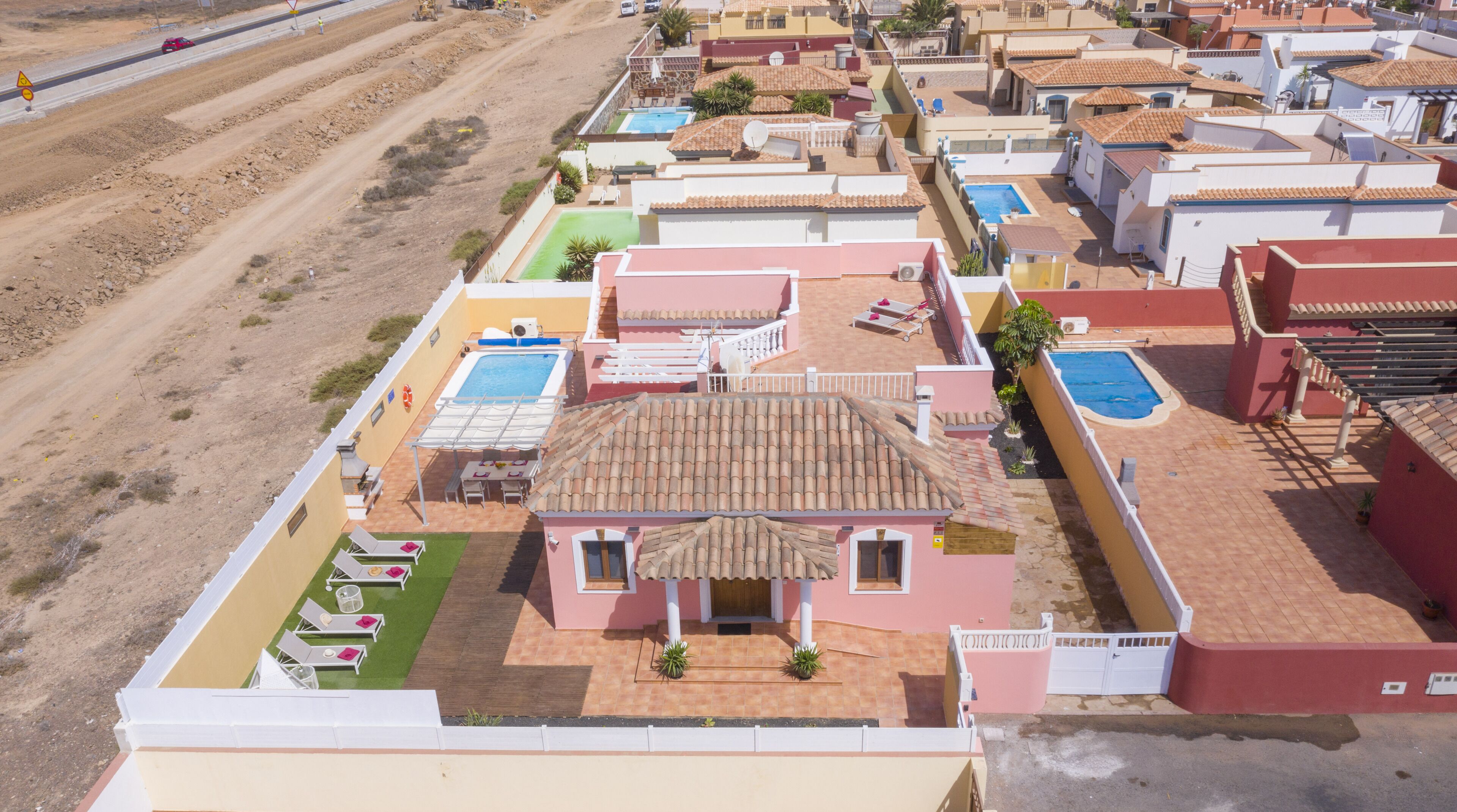 Et boligområde med flere huse, hvert med swimmingpool, overdækket terrasse og en lille have.