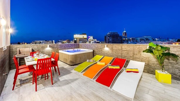 Une terrasse sur le toit comprenant un espace repas, un jacuzzi et des tapis de salon aux couleurs vives.