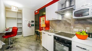 Une cuisine moderne avec des armoires blanches, un mur d’accent rouge, un four à micro-ondes encastré et un saladier de pommes vertes posé sur le comptoir.