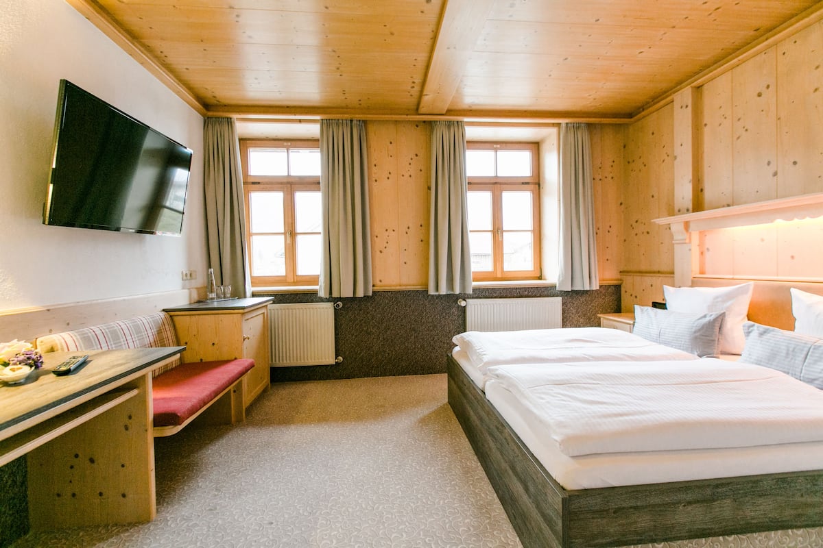 Ein Hotelzimmer mit einem Bett, einem Schreibtisch mit Stuhl, einem an der Wand befestigten Fernseher und einem fenster mit Vorhängen.