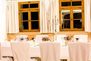 Une table à manger dressée pour un événement formel, avec des nappes blanches, des chaises et des centres de table floraux.