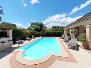 Una piscina rectangular con borde de azulejos, rodeada de sillones de descanso y una zona de estar cubierta.