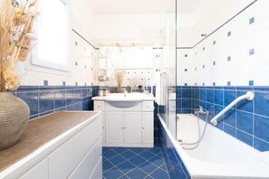 Un baño con un lavamanos blanco, paredes cubiertas de azulejos azules y una bañera blanca.
