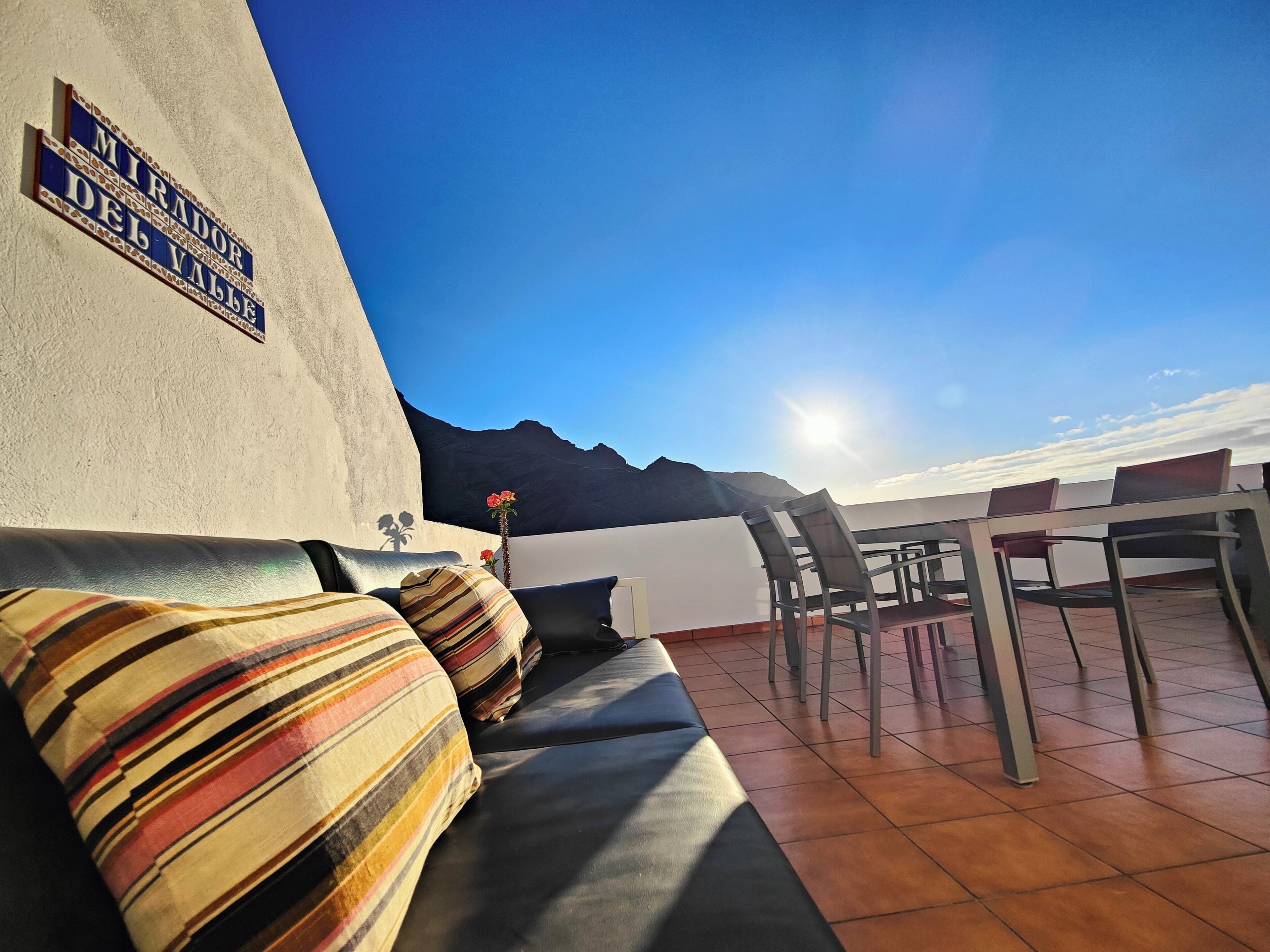 Una terraza con un sofá y sillas, un letrero que dice "MIRADOR DEL VALLE", y vista a la montaña.