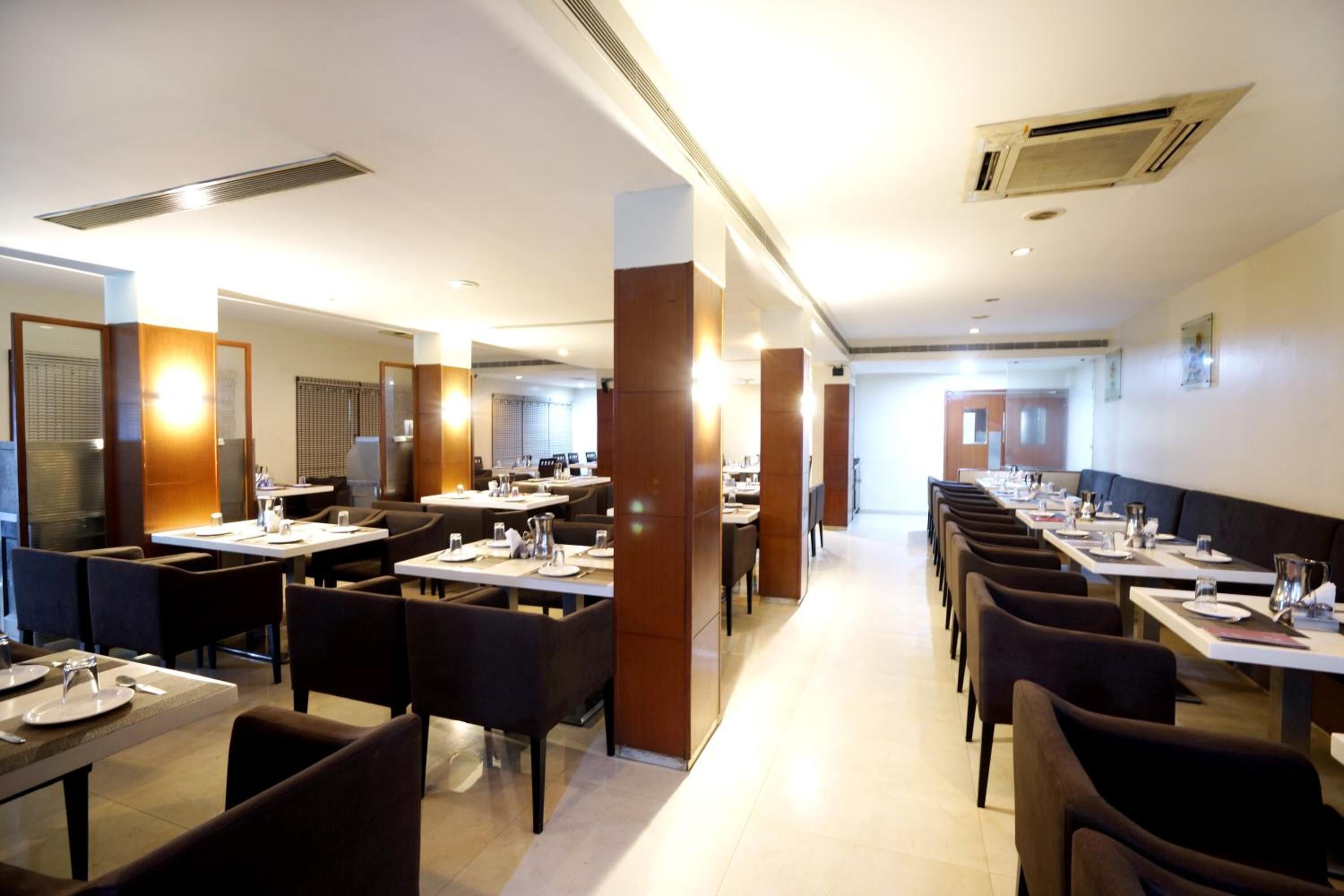 A modern restaurant with long tables and booths, a central column, and a bright, well-lit interior.