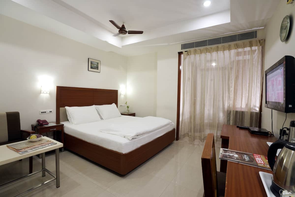 Habitación de hotel con una cama grande, un escritorio con silla, televisión y ventilador de techo.