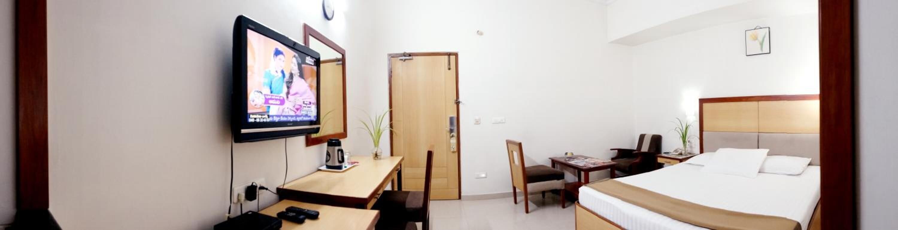 A hotel room with a bed, a desk with a chair, a television, and a wooden door.