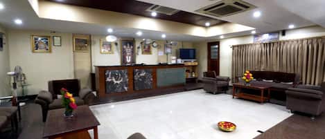 A hotel lobby with a reception desk, seating area, and a television.