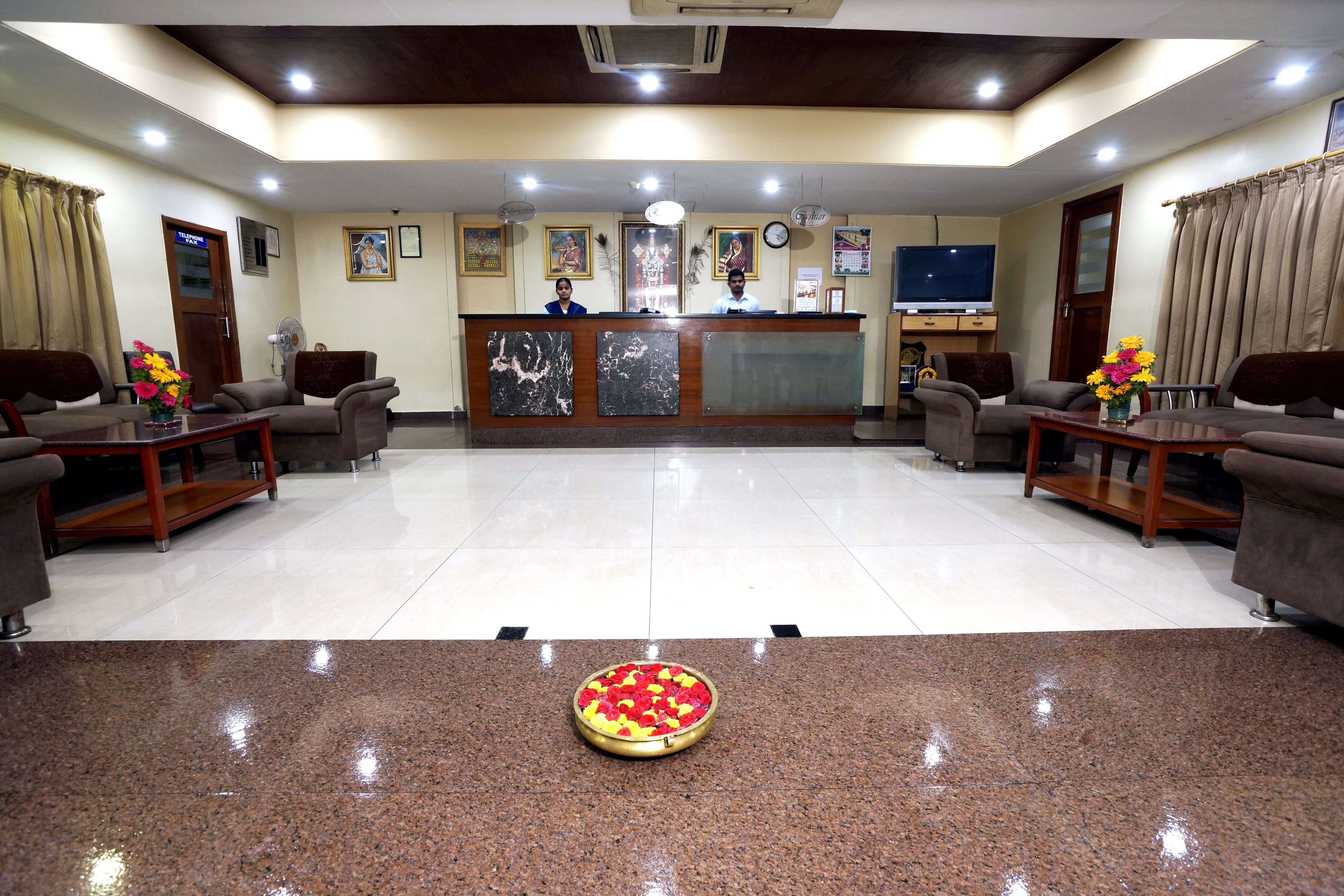 A hotel reception area with a marble reception desk, two sofas, a coffee table, and a decorative flower arrangement on the floor.