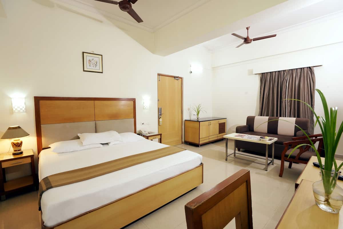 Una habitación de hotel con una cama grande, un escritorio, un sofá, un ventilador de techo y una puerta.