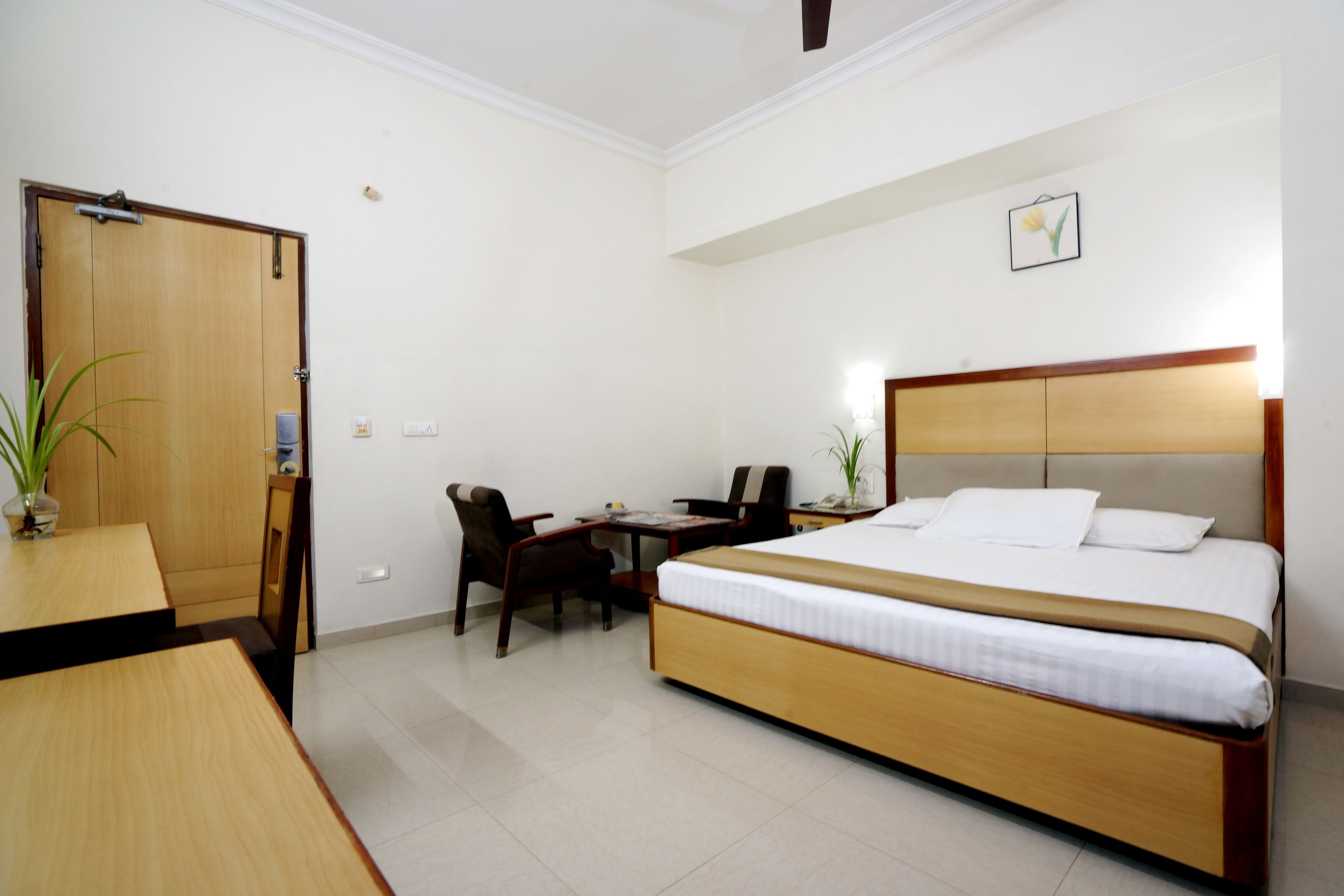 A hotel room with a bed, desk, chairs, and a door.