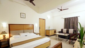 Une chambre d’hôtel avec un grand lit, un bureau, un canapé, un ventilateur de plafond et une porte.