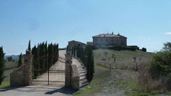 A stone building with a gated entrance, surrounded by cypress trees and a gravel path leading to it.