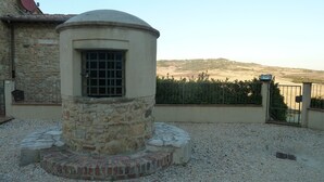 A stone structure with a window, surrounded by gravel and a metal fence. - Apartment in Beautifully Restored Medieval Tuscan Village, 7klm from Volterra (Pisa)