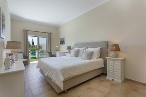 Quarto com cama, mesas de cabeceira, escrivaninha e vista para o exterior.