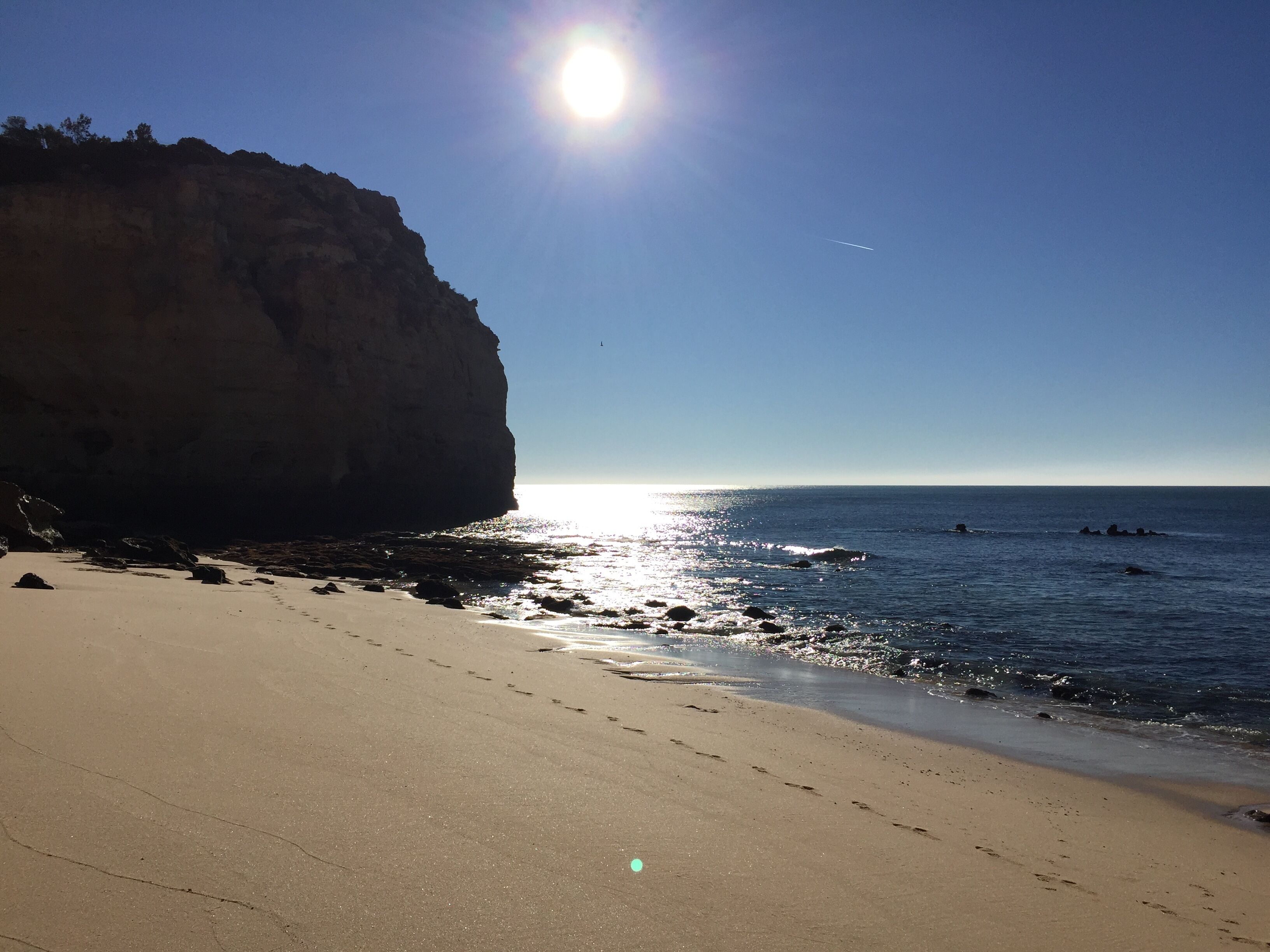 Une plage avec une grande formation rocheuse, un ciel dégagé et une mer calme.