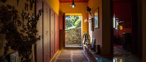 Un pasillo con suelo de piedra, puertas de madera y un jarrón con flores secas.