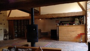 Una habitación acogedora con vigas de madera a la vista, chimenea, zona de bar y espacio de descanso con cojines.