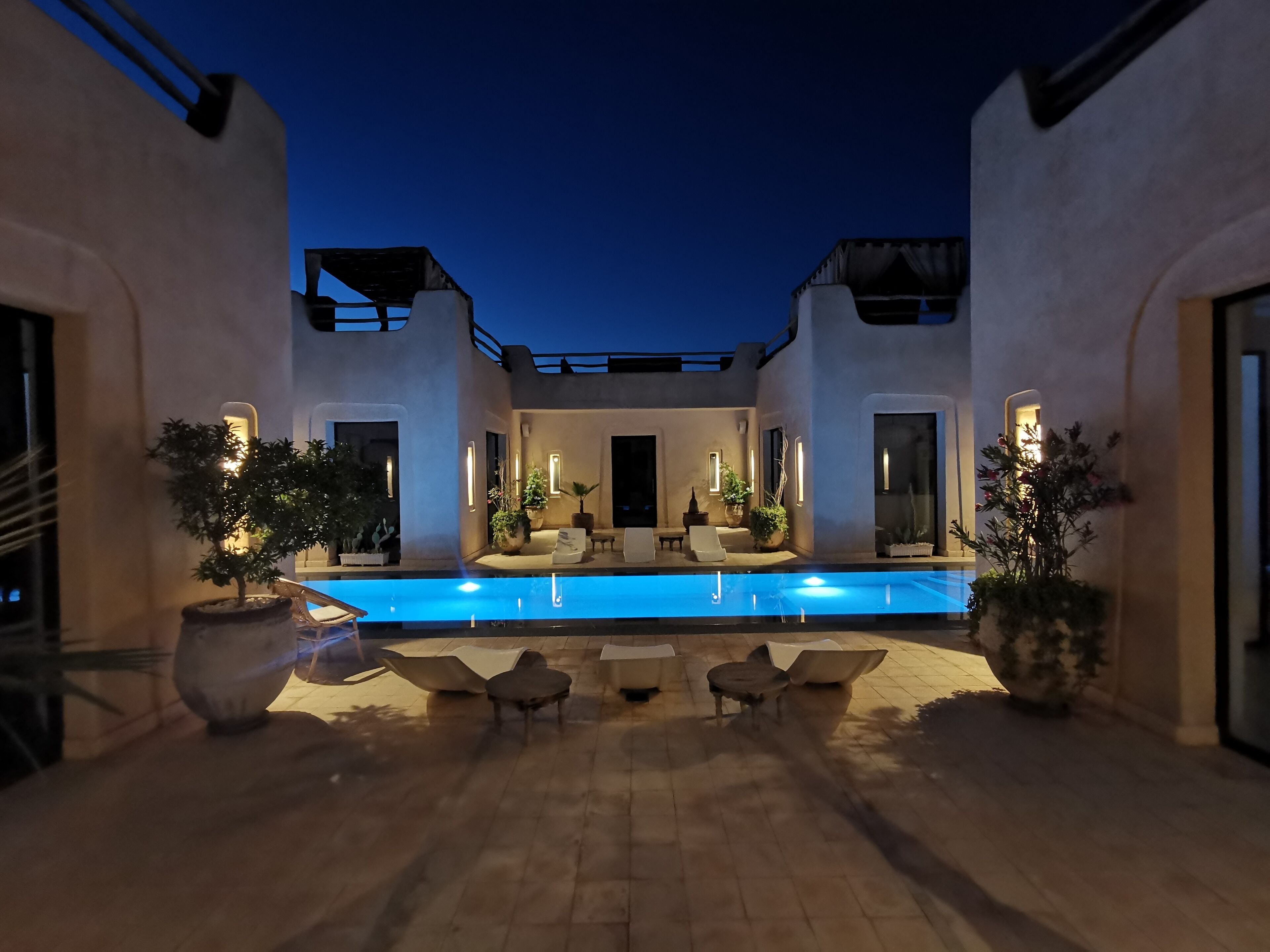 A pool area with a rectangular pool, lounge chairs, and potted plants.