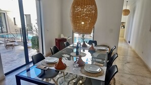 Un coin repas avec une table en verre, des chaises noires et un luminaire suspendu en fibres tressées.