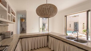 Une cuisine moderne dotée d’un grand îlot central, d’un luminaire suspendu et offrant une vue sur une piscine.