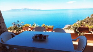 Una mesa con una bandeja de bebidas, sillas blancas y vista al mar.