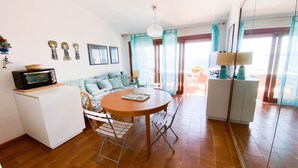 Un espacio habitable compacto con kitchenette, comedor y zona de estar con sofá y sillones.