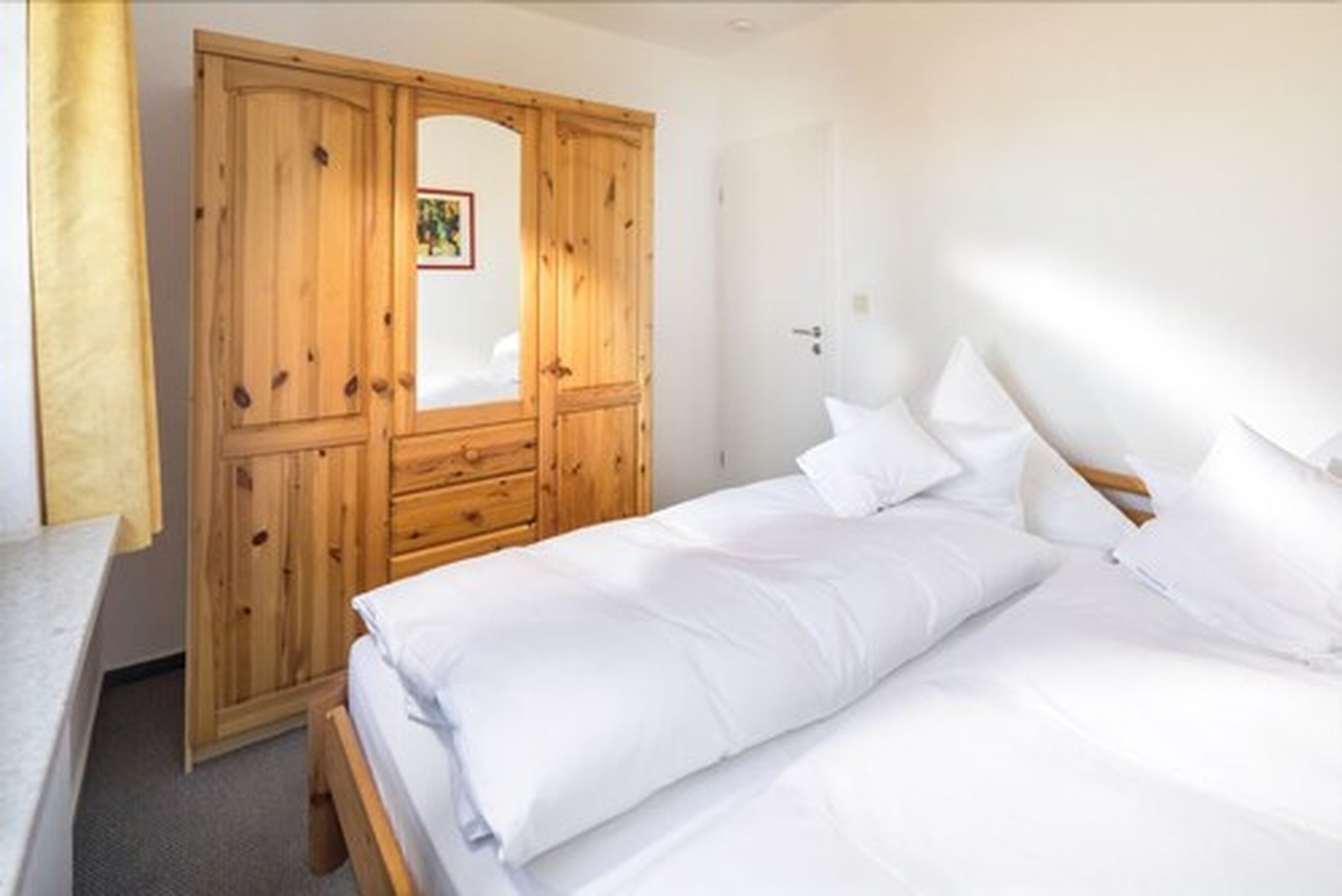 A bedroom with a wooden wardrobe, a bed with white bedding, and a door with a small picture.