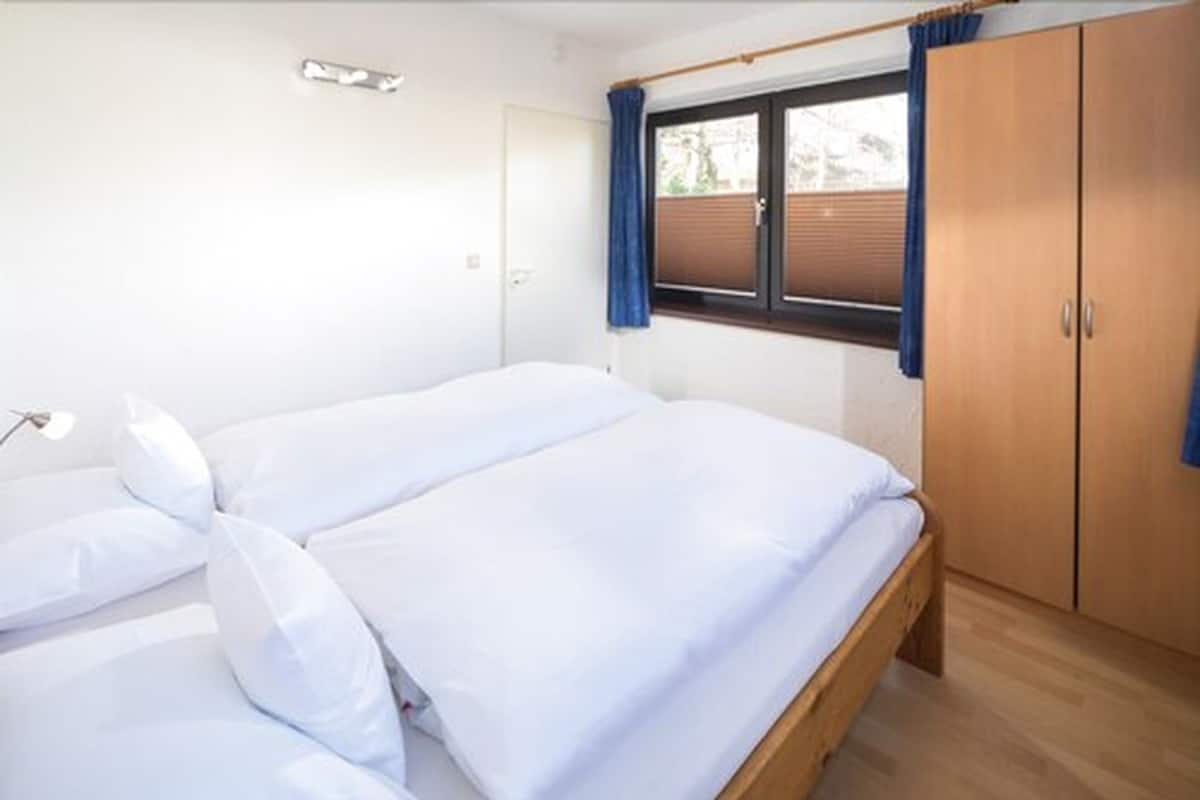 A bedroom with a double bed, wooden wardrobe, and a window with curtains.