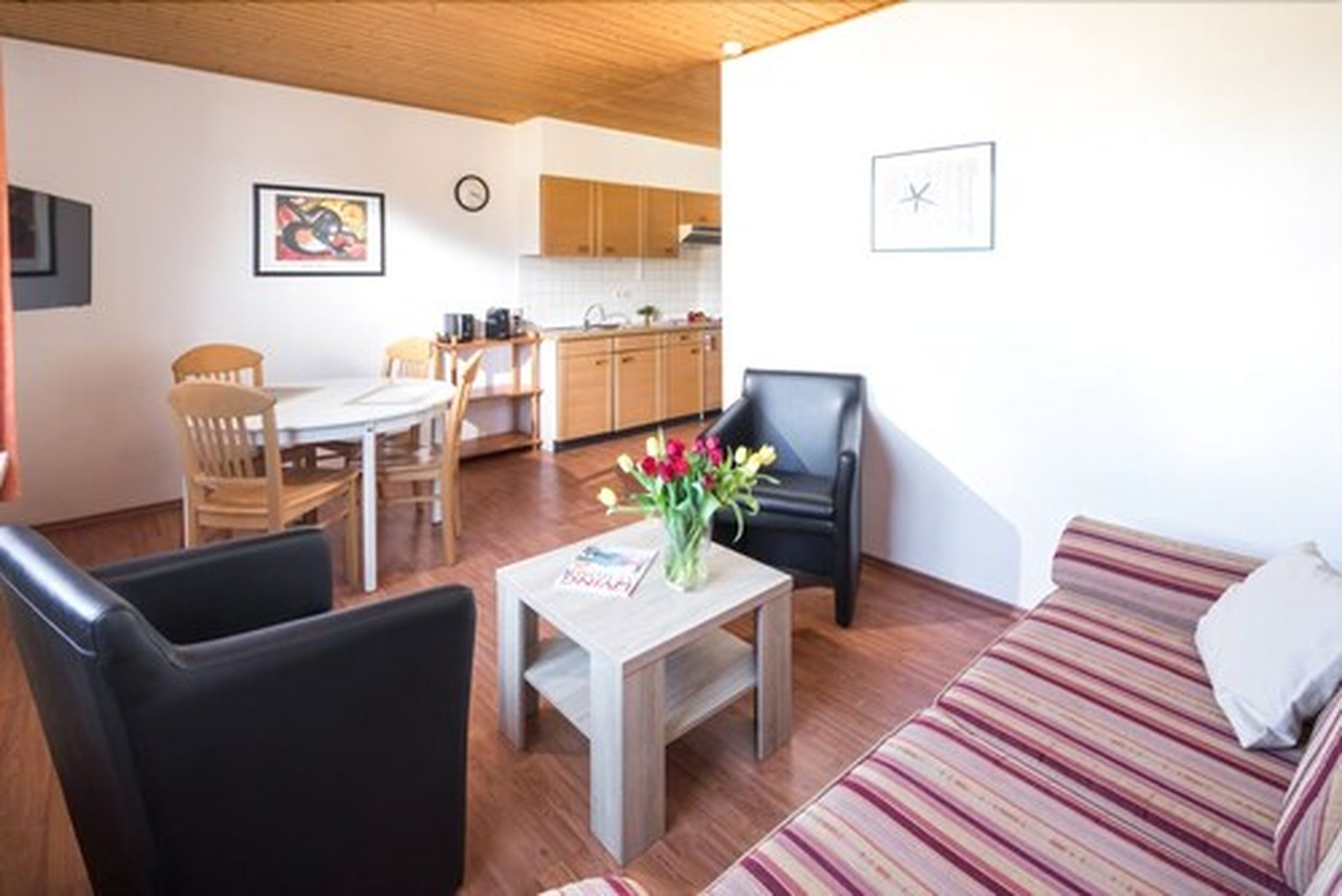 Un salon comprenant un canapé, une table basse avec un vase, et un coin repas avec des chaises et une table.