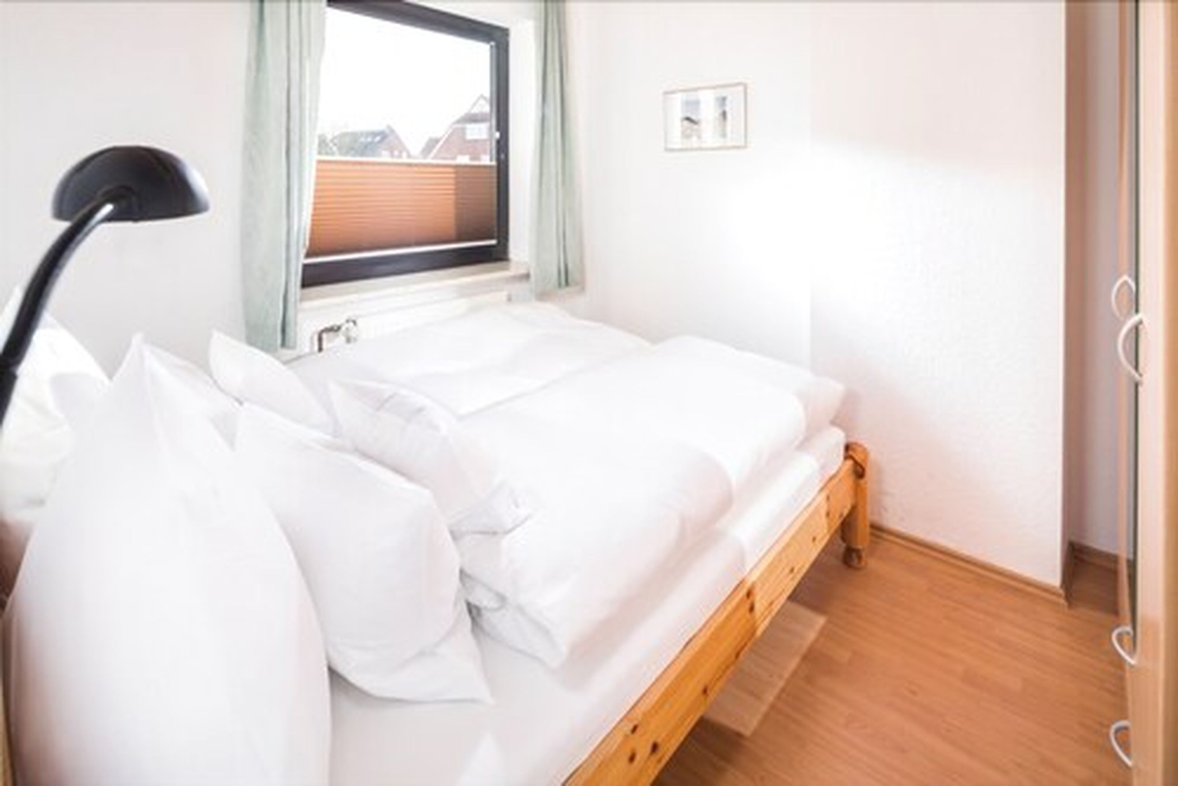 A single bed with white bedding in a room with wooden flooring and a window with a view of buildings outside.