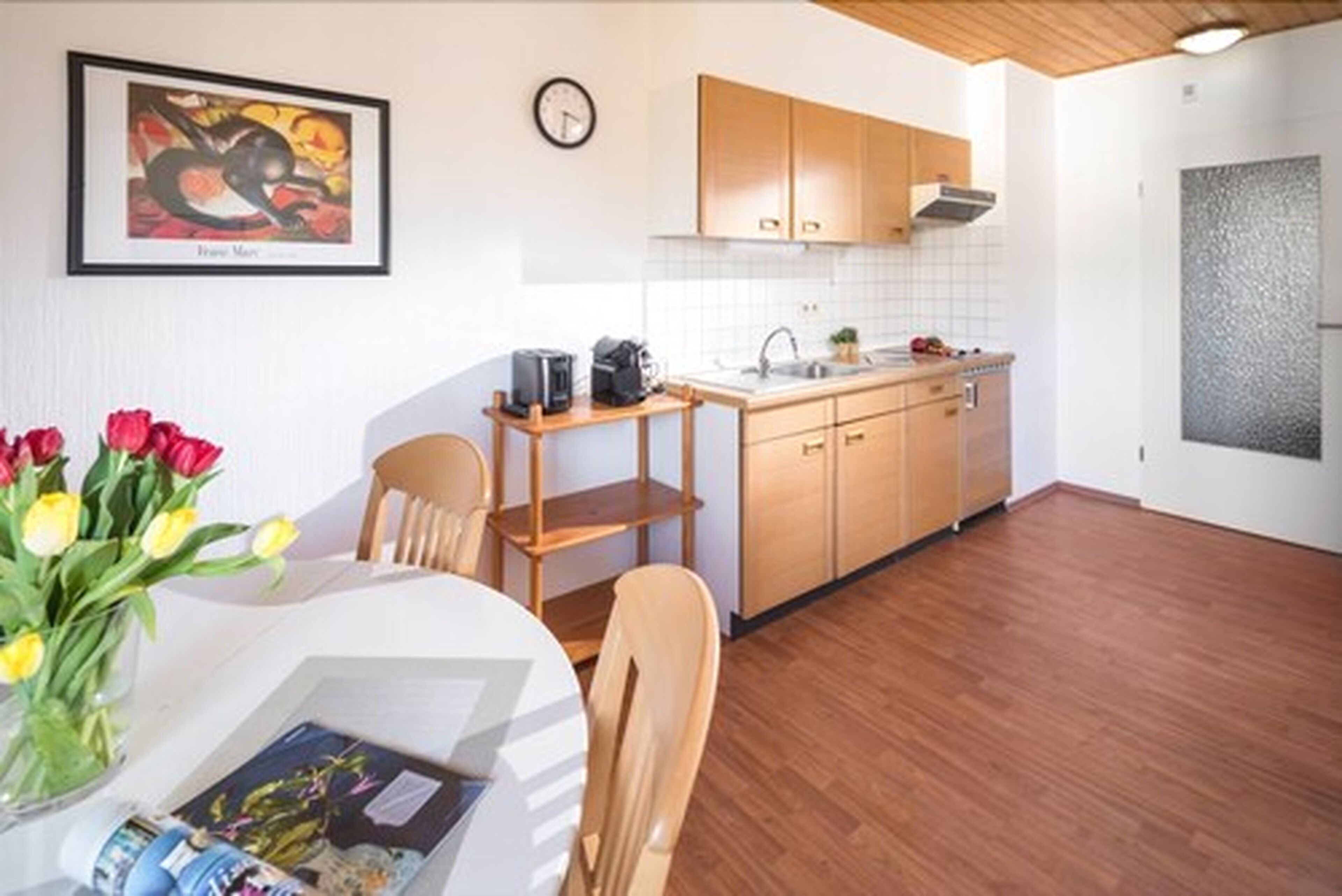 A modern kitchen with wooden cabinets, a white countertop, and a clock on the wall.