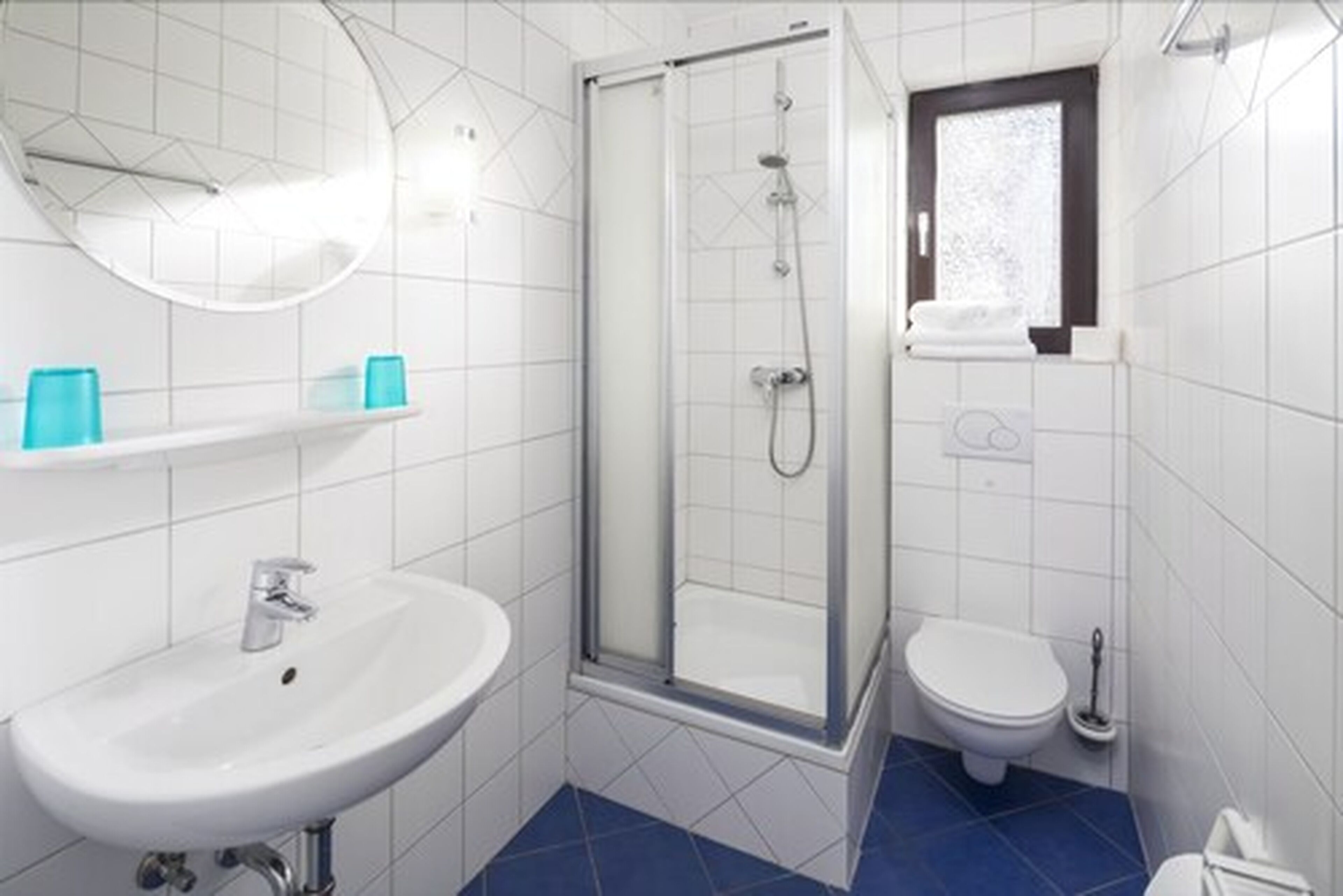 Une salle de bain avec un lavabo blanc, une douche à parois de verre, des toilettes et une fenêtre.