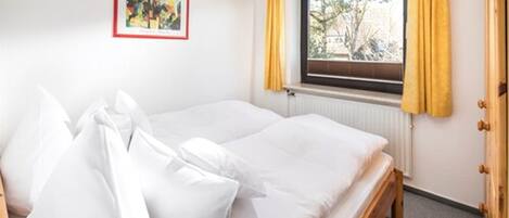 A single-bed room with a window, a radiator, and a framed picture on the wall.