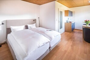 A bedroom with a double bed, a bedside table, a lamp, and a view of a bathroom and kitchen area. - Birkenhof (Norderney)