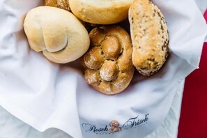 A basket of various baked goods, including a braided bread and a sesame seed roll, on a white paper with a logo.